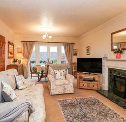 A living room with floral sofas a television on a wooden stand and a fireplace at Sanderling in Scalby