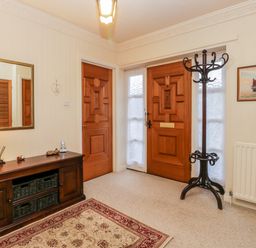 An entryway with wooden front and interior doors a wooden cabinet with a lamp and mirror a coat rack and a rug at Sanderling in Scalby