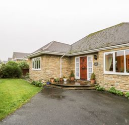 A stone house with a wooden front door potted plants a driveway and a grass lawn at Sanderling in Scalby