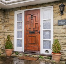 A wooden front door with decorative glass panels on a stone wall with potted plants outside at Sanderling in Scalby