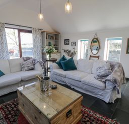 A living room with two white sofas and a wooden coffee table with a bottle in a bucket and glasses at Cwch Gwenyn in Llanfachraeth
