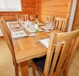 A wooden dining table with six chairs set with placemats glasses cutlery and a bottle in a room with wooden walls at Watersview Lodge in Rudyard near Leek