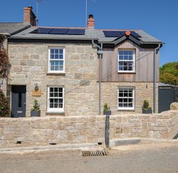 A stone cottage with solar panels on the roof and a stone wall in front at Stargazy Cottage in Praa Sands