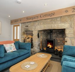 A living room with stone fireplace wood burning stove two blue sofas and a wooden coffee table at Stargazy Cottage Praa Sands