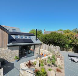 An outdoor patio area with stone walls and plants two lounge chairs with orange cushions and a sofa with orange cushions at Stargazy Cottage in Praa Sands