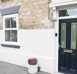 A front door with frosted glass panels and a white window with blinds on a stone and painted wall with a flower pot in front at Potter Hill Cottage in Pickering