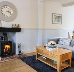 A living room with a wood burning stove a wooden coffee table and a grey sofa at Potter Hill Cottage Pickering