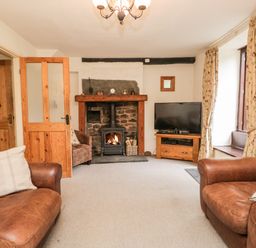 A living room with leather sofas a fireplace a television and floral curtains at Beckfold Cottage in Broughton In Furness