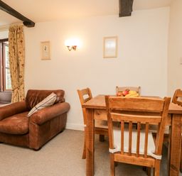 A room with a brown leather armchair a wooden dining table with four chairs and fruit on top at Beckfold Cottage in Broughton-In-Furness
