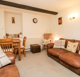 A living room with brown leather sofas wooden dining table and chairs a wall clock and a rocking chair at Beckfold Cottage in Broughton-In-Furness