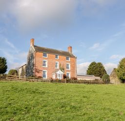 A brick house with white framed windows and two chimneys on a grassy hill at Squires Rest in Llanfair Caereinion