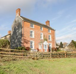 A three-story brick house with multiple chimneys and a wooden fence around the garden at Squires Rest in Llanfair Caereinion