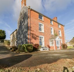 A three-story brick house with multiple windows and a small front porch surrounded by bushes and driveway at Squires Rest in Llanfair Caereinion