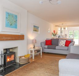 A living room with a fireplace two grey sofas with red cushions a small white table and kitchen in the background at Sisial-Y-Mor in Rhosneigr