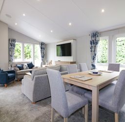 A living room and dining area with grey upholstered chairs a wooden dining table blue armchair and sofa with cushions at Pinehurst Lodge in St Day