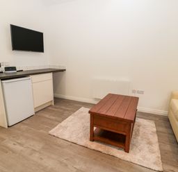 A small living area with a mounted television wooden coffee table beige sofa and mini fridge at The Old Stables in Belford