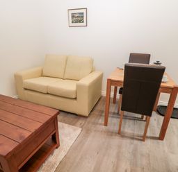 A small room with a beige loveseat sofa a wooden coffee table a dining table with two chairs and a framed picture on the wall at The Old Stables in Belford