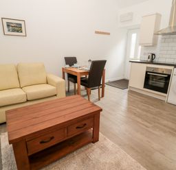 A living area with a beige sofa a wooden coffee table a small dining table with two chairs and a kitchen with appliances at The Old Stables in Belford