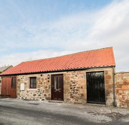 A stone building with red tiled roof and doors on a paved street at The Old Stables in Belford