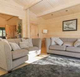 A living room with two grey sofas with patterned cushions a floor lamp a framed picture on a wooden wall and a grey rug at Gardener's Lodge in Huby