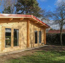 A wooden cabin with glass doors and a green garden at Gardener's Lodge in Huby