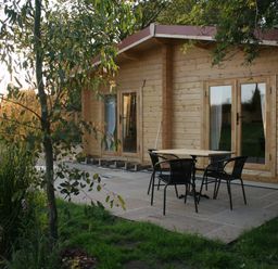 A wooden cabin with glass doors and a patio with table and four chairs surrounded by trees at Gardeners Lodge in Huby