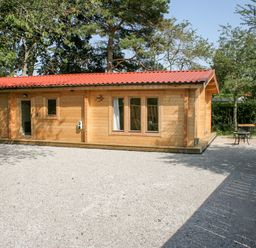 A wooden cabin with red roof on a gravel driveway surrounded by trees at Gardeners Lodge in Huby