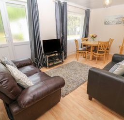 A living room with two leather sofas a small TV on a stand a round dining table with chairs and a coat rack at 11 Tremore in Liskeard