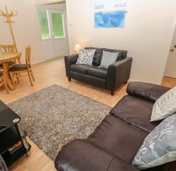 A living room with two leather sofas a wooden dining table with chairs a coat rack and a rug at 11 Tremore in Liskeard