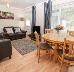 A living room with two leather sofas a round wooden dining table with chairs and a vase of flowers at 11 Tremore in Liskeard