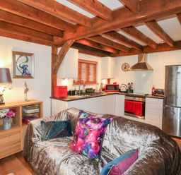 A kitchen and seating area with wooden beams white cabinets and colorful cushions at Honeypot Lodge in Camelford