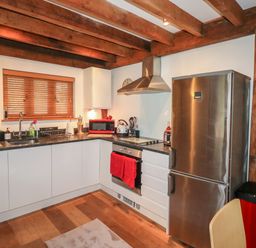 A kitchen with wooden beams white cabinets stainless steel appliances and wooden floor at Honeypot Lodge in Camelford