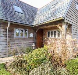 Exterior of a wooden house with plants and shrubs near the entrance at Honeypot Lodge in Camelford