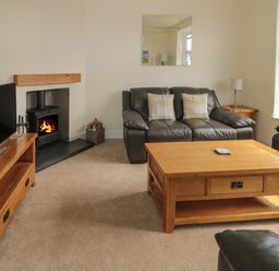 A living room with black leather sofas a wooden coffee table a wooden TV stand with a flat screen TV and a fireplace at Hazonleigh in Seahouses