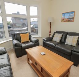 A living room with leather sofas a wooden coffee table a floor lamp and a framed picture on the wall at Hazonleigh in Seahouses