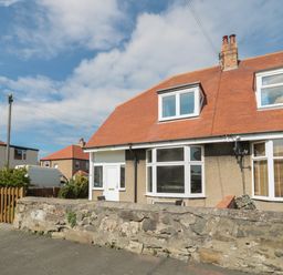 A semi detached house with a red roof and stone wall in front at Hazonleigh in Seahouses