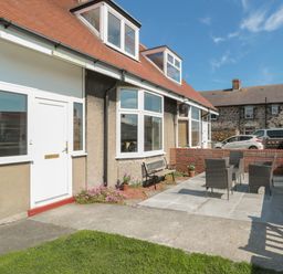 A front yard patio with outdoor chairs and a bench in front of a house at Hazonleigh in Seahouses