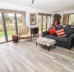 A living room with a gray sofa and red pillows an armchair a patterned ottoman and sliding glass doors overlooking a garden at Romsey Lodge in Wark