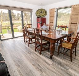 A dining room with a wooden table and six chairs next to sliding glass doors and a window with wooden shutters at Romsey Lodge in Wark