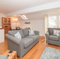 A living room with grey sofas and a wooden floor next to a dining area and kitchen at 42 Dart Marina in Dartmouth