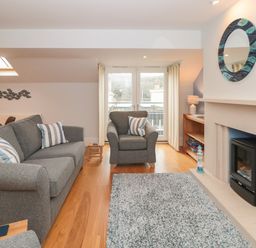 A living room with a gray sofa and armchair a fireplace and glass doors at 42 Dart Marina in Dartmouth