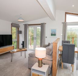 A living room with a sofa table lamp television and dining table with chairs at 1 Valley View in Lanreath