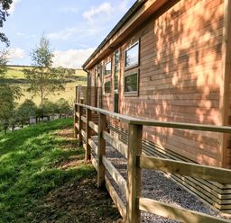 An exterior view of a wooden house with a fenced path and grassy hillside in the background at 1 Valley View in Lanreath