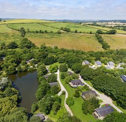 A countryside area with a lake surrounded by trees and multiple houses with roads in the greenery at 1 Valley View in Lanreath