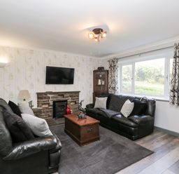 A living room with two black leather sofas cushions a wooden chest coffee table a mounted television and a large window at Pool House in The Narth near Trellech