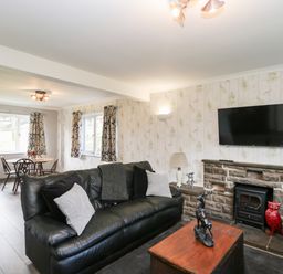 A living room with a leather sofa and a wood table with sculpture a wall-mounted television above a stone fireplace at Pool House in The Narth near Trellech