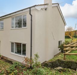 The exterior of a two-story house with white walls and multiple windows surrounded by grass and plants at Pool House The Narth near Trellech