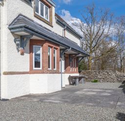 Exterior of a house with gravel and paved patio area next to a stone wall with bare trees in the background at Keepers Cottage in Hawkshead