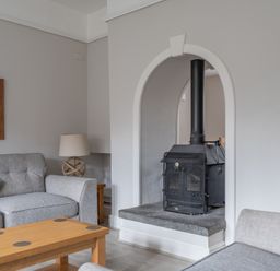 A living room with a wood burning stove a gray sofa a wooden coffee table and a table lamp at Keepers Cottage Hawkshead