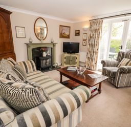 A living room with striped sofa and armchair a wooden coffee table and fireplace at Rosemead in Moreton-In-Marsh